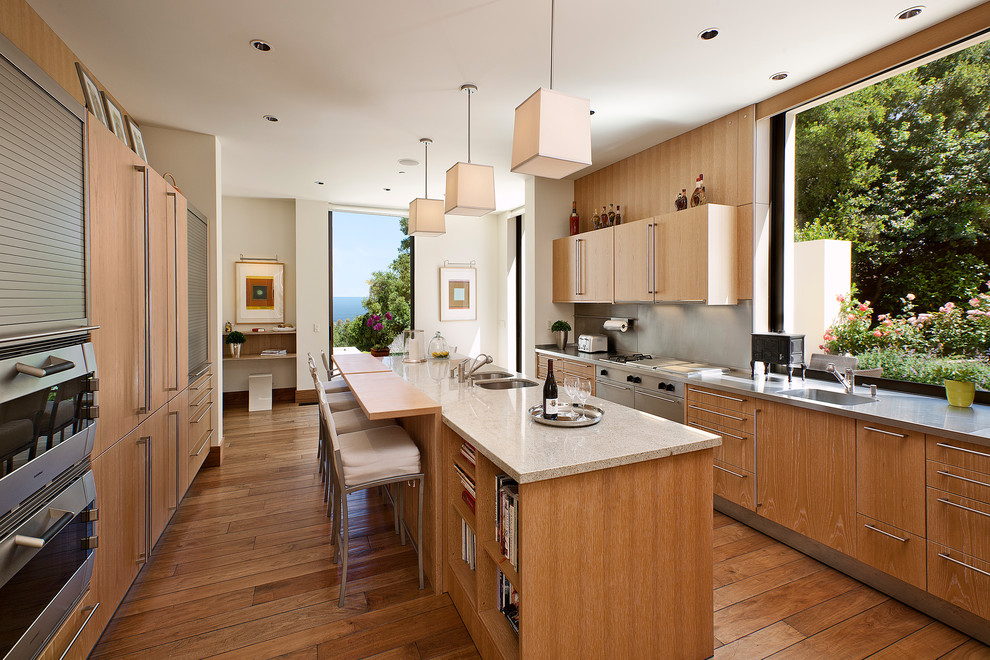 Große Mediterrane Küche mit hellbraunen Holzschränken, Küchengeräten aus Edelstahl, Kücheninsel, grauer Arbeitsplatte, Waschbecken, flächenbündigen Schrankfronten, Küchenrückwand in Grau und braunem Holzboden in Santa Barbara
