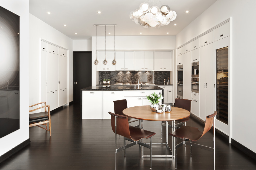 Modern inredning av ett kök och matrum, med släta luckor, vita skåp, rostfria vitvaror, mörkt trägolv och en köksö