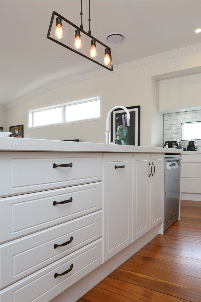 Medium sized traditional l-shaped open plan kitchen in Auckland with a submerged sink, shaker cabinets, white cabinets, engineered stone countertops, white splashback, metro tiled splashback, stainless steel appliances, light hardwood flooring, an island and multi-coloured floors.