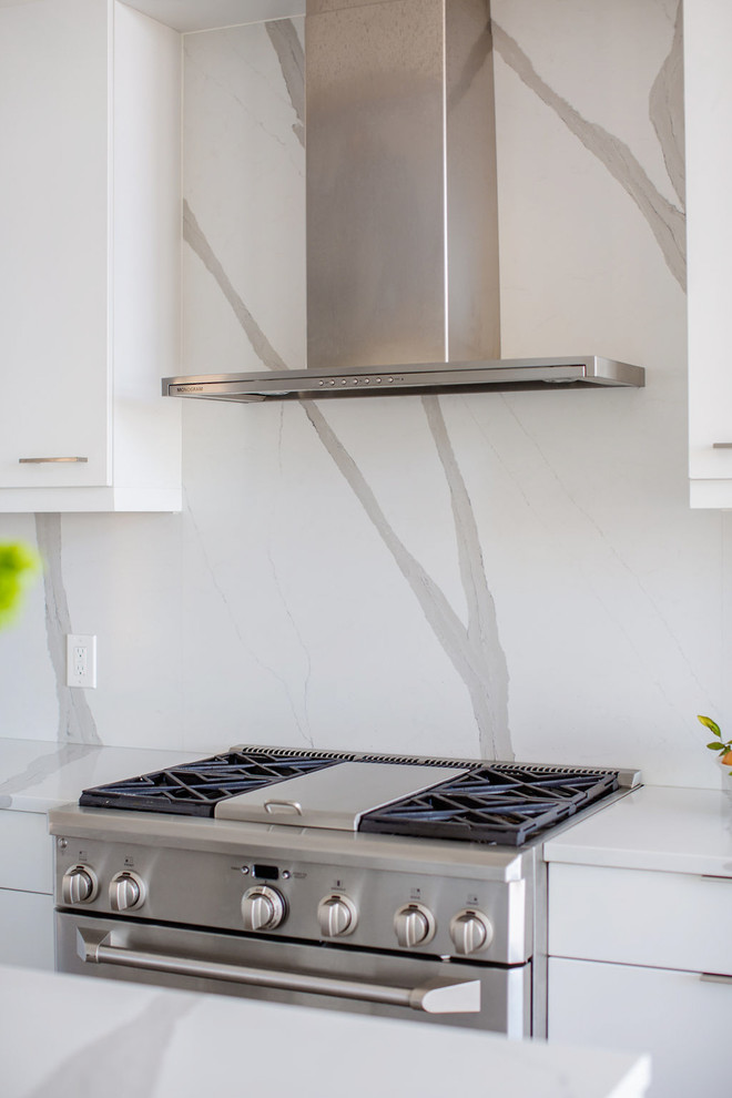 Modern inredning av ett mellanstort vit vitt kök, med en undermonterad diskho, släta luckor, vita skåp, bänkskiva i kvarts, vitt stänkskydd, stänkskydd i sten, rostfria vitvaror, ljust trägolv, en köksö och grått golv
