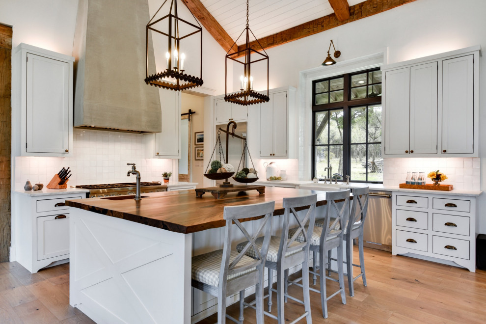 Inspiration for a rustic l-shaped light wood floor, beige floor, exposed beam, shiplap ceiling and vaulted ceiling kitchen remodel in Austin with a farmhouse sink, shaker cabinets, white cabinets, white backsplash, stainless steel appliances, an island and white countertops