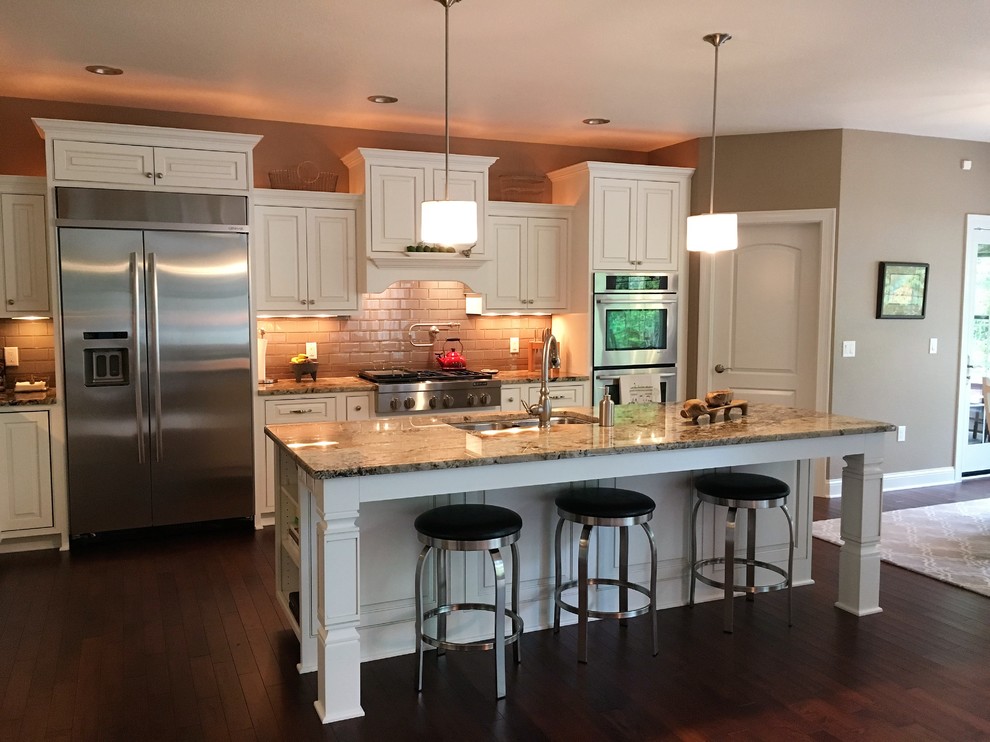 Example of a large transitional l-shaped dark wood floor and brown floor open concept kitchen design in Milwaukee with a double-bowl sink, raised-panel cabinets, white cabinets, granite countertops, brown backsplash, subway tile backsplash, stainless steel appliances and an island