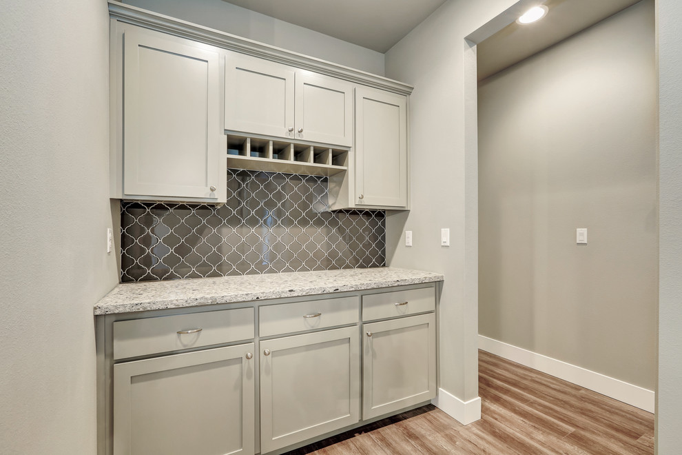 Cette image montre une cuisine design avec un placard à porte shaker, des portes de placard grises, un plan de travail en granite, une crédence grise et une crédence en carreau de verre.