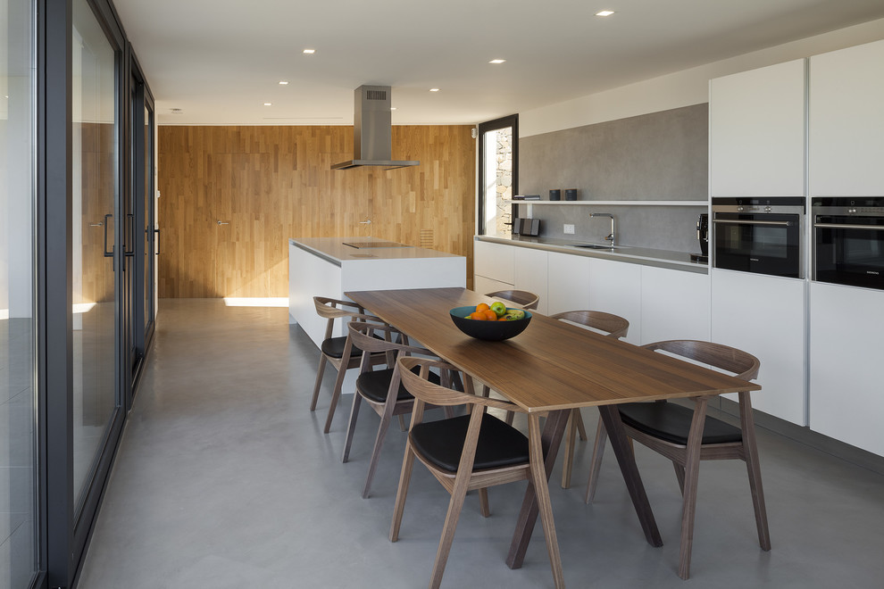 Modern inredning av ett stort kök, med betonggolv, en undermonterad diskho, släta luckor, vita skåp, bänkskiva i koppar, grått stänkskydd, rostfria vitvaror och en köksö