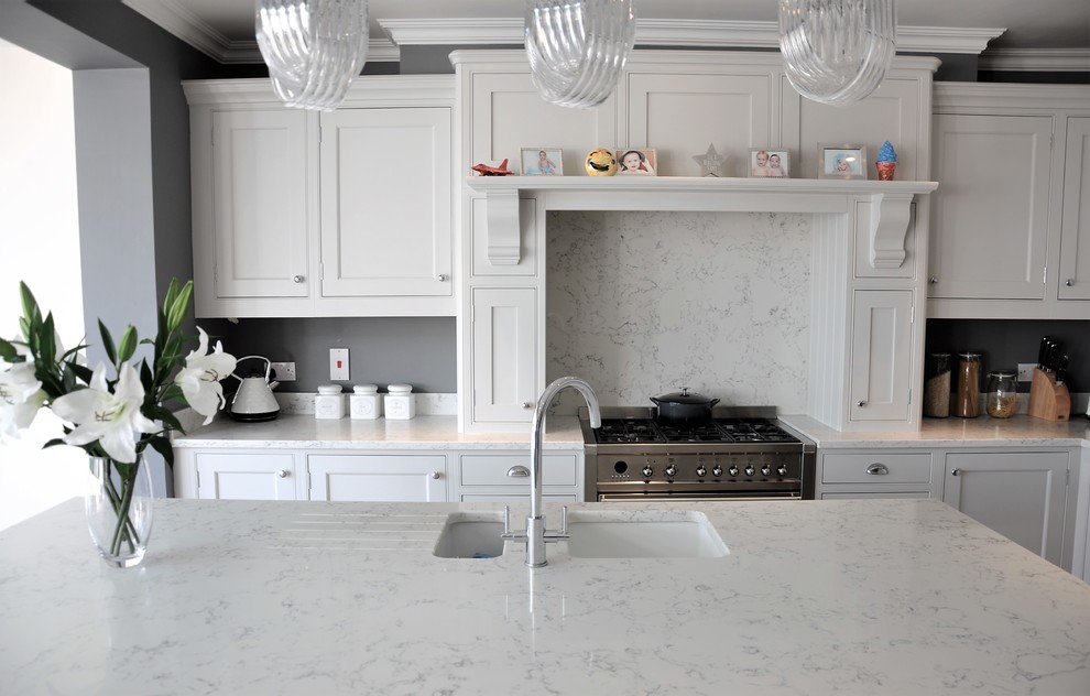 Klassisk inredning av ett stort vit vitt kök, med en dubbel diskho, skåp i shakerstil, grå skåp, bänkskiva i kvartsit, vitt stänkskydd, stänkskydd i sten, rostfria vitvaror, laminatgolv, en köksö och brunt golv