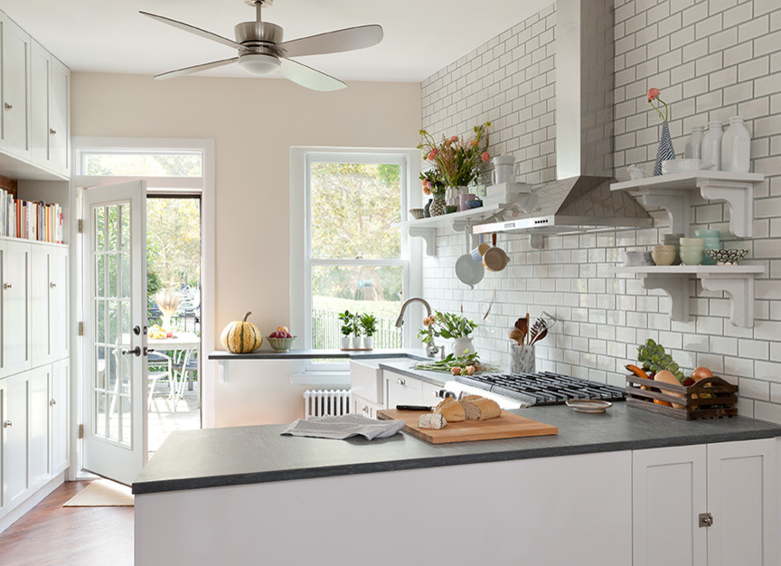 Design ideas for a small rural l-shaped kitchen/diner in New York with a belfast sink, shaker cabinets, white cabinets, soapstone worktops, white splashback, metro tiled splashback, stainless steel appliances, medium hardwood flooring and a breakfast bar.
