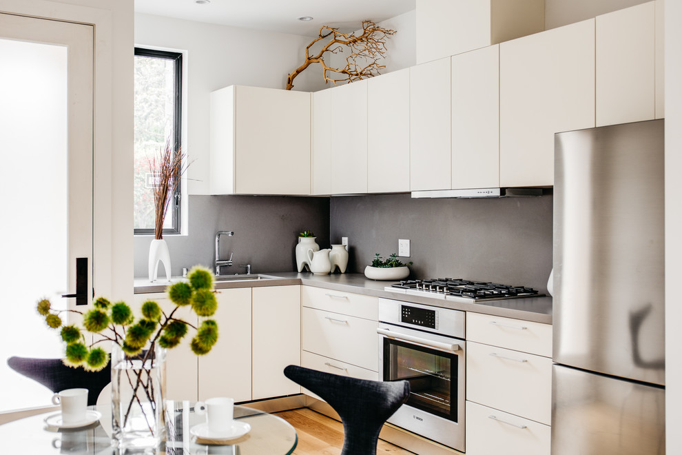 Inredning av ett modernt mellanstort grå grått kök, med en undermonterad diskho, släta luckor, vita skåp, bänkskiva i koppar, grått stänkskydd, stänkskydd i sten, rostfria vitvaror och ljust trägolv