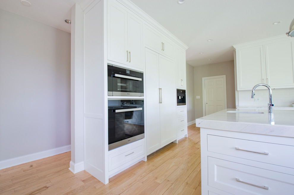 Exempel på ett stort minimalistiskt vit vitt kök, med en undermonterad diskho, vita skåp, bänkskiva i kvartsit, vitt stänkskydd, stänkskydd i keramik, rostfria vitvaror, ljust trägolv och en köksö