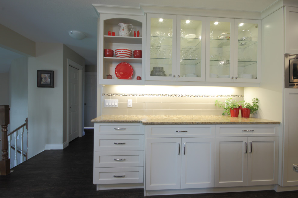 Example of a mid-sized trendy u-shaped dark wood floor and brown floor eat-in kitchen design in Other with an undermount sink, shaker cabinets, white cabinets, granite countertops, stainless steel appliances, an island and white backsplash