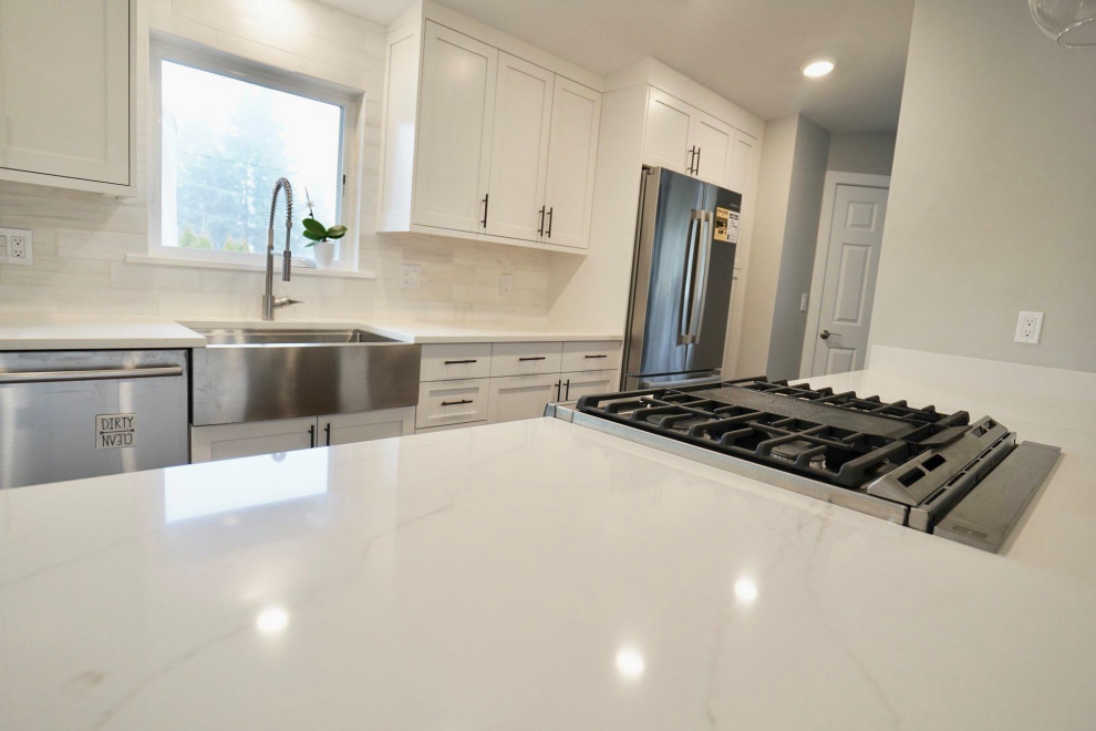 This is an example of a large modern kitchen in Seattle with a belfast sink, shaker cabinets, white cabinets, marble worktops, white splashback, ceramic splashback, stainless steel appliances, medium hardwood flooring, an island and white worktops.