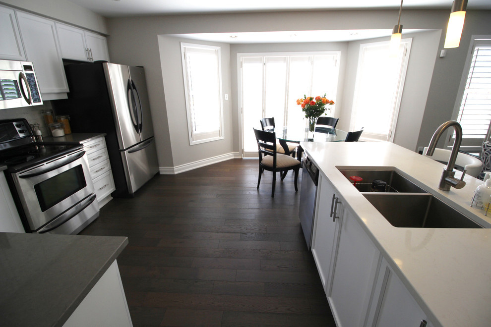 Example of a trendy medium tone wood floor open concept kitchen design in Toronto with an undermount sink, recessed-panel cabinets, white cabinets, quartz countertops, stainless steel appliances, white backsplash and an island