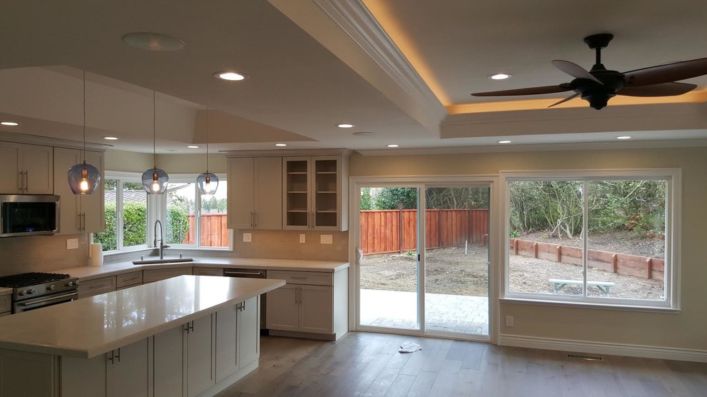 This is an example of a medium sized contemporary l-shaped kitchen/diner in San Francisco with a double-bowl sink, shaker cabinets, white cabinets, composite countertops, stainless steel appliances, dark hardwood flooring, an island and brown floors.