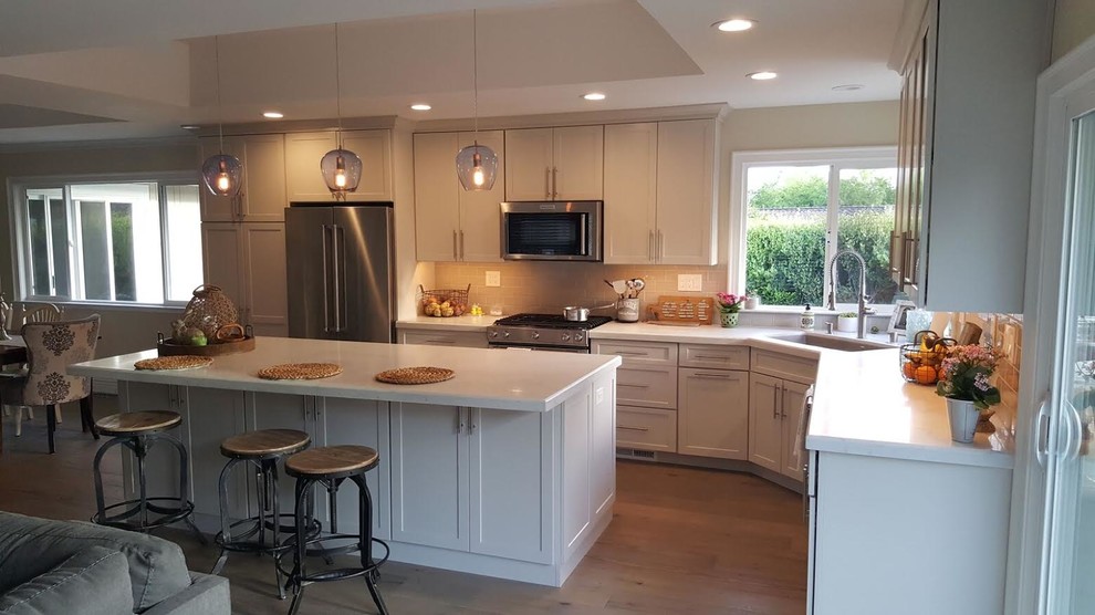Photo of a medium sized contemporary l-shaped kitchen/diner in San Francisco with a double-bowl sink, shaker cabinets, white cabinets, composite countertops, stainless steel appliances, dark hardwood flooring, an island and brown floors.