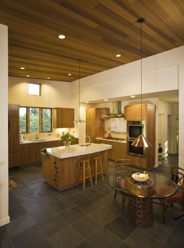 Imagen de cocina actual con electrodomésticos de acero inoxidable, armarios con paneles lisos, puertas de armario de madera clara y barras de cocina