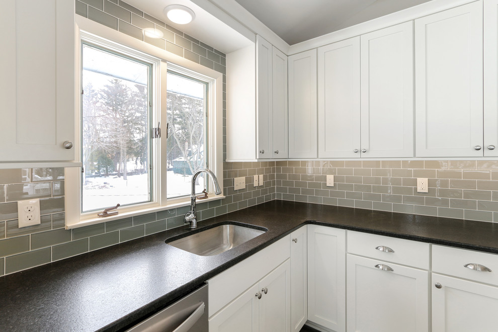 Inspiration for a mid-sized coastal u-shaped vinyl floor and beige floor eat-in kitchen remodel in Milwaukee with an undermount sink, white cabinets, granite countertops, gray backsplash, ceramic backsplash, stainless steel appliances, a peninsula, black countertops and shaker cabinets