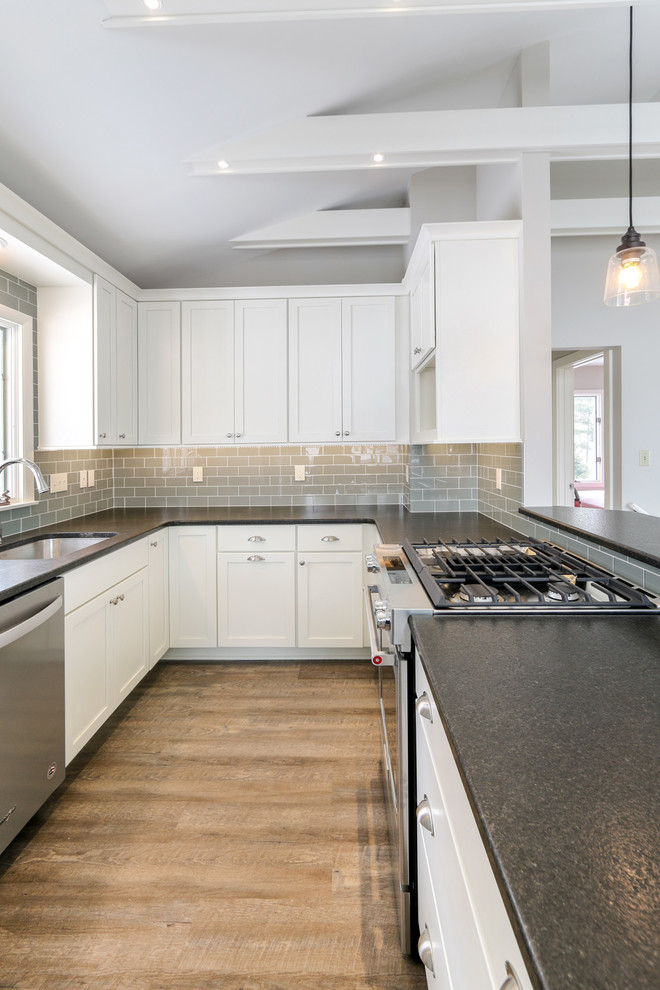 Example of a mid-sized beach style u-shaped vinyl floor and beige floor eat-in kitchen design in Milwaukee with an undermount sink, white cabinets, granite countertops, gray backsplash, ceramic backsplash, stainless steel appliances, a peninsula, black countertops and shaker cabinets