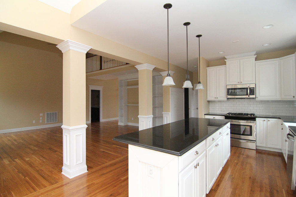 Inspiration for a large country l-shaped medium tone wood floor open concept kitchen remodel in Raleigh with a farmhouse sink, raised-panel cabinets, white cabinets, granite countertops, white backsplash, ceramic backsplash, stainless steel appliances and an island