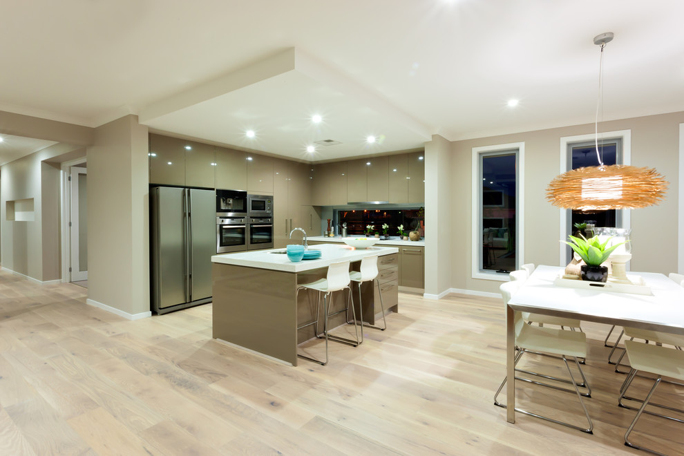 This is an example of a large contemporary l-shaped open plan kitchen in Toronto with a submerged sink, flat-panel cabinets, beige cabinets, engineered stone countertops, window splashback, stainless steel appliances, light hardwood flooring, an island and beige floors.