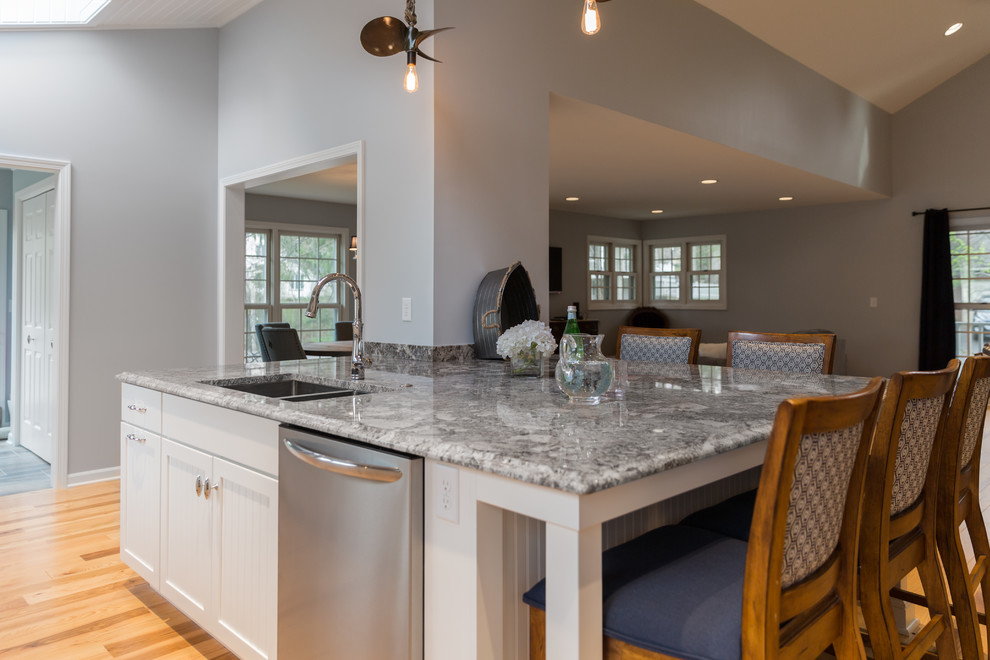 Transitional medium tone wood floor kitchen photo in Milwaukee with white cabinets, gray backsplash, porcelain backsplash, stainless steel appliances, an undermount sink, flat-panel cabinets and an island