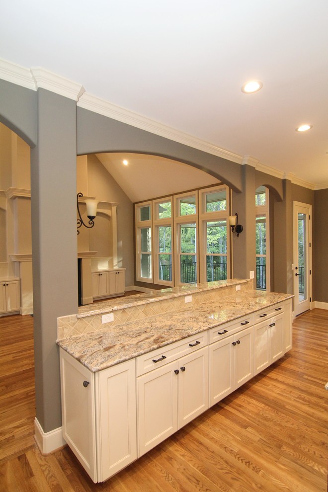 Inspiration for a large timeless u-shaped medium tone wood floor open concept kitchen remodel in Raleigh with an undermount sink, recessed-panel cabinets, white cabinets, granite countertops, beige backsplash, ceramic backsplash, stainless steel appliances and two islands