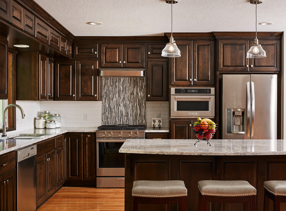 Example of a mid-sized classic l-shaped medium tone wood floor kitchen design in Minneapolis with an undermount sink, raised-panel cabinets, dark wood cabinets, multicolored backsplash, matchstick tile backsplash, stainless steel appliances, an island and multicolored countertops