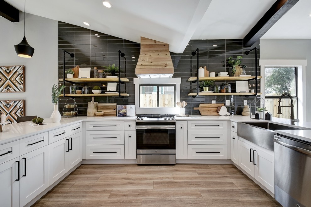 Example of a mid-sized trendy u-shaped brown floor kitchen design in Austin with a farmhouse sink, shaker cabinets, white cabinets, black backsplash, stainless steel appliances and white countertops