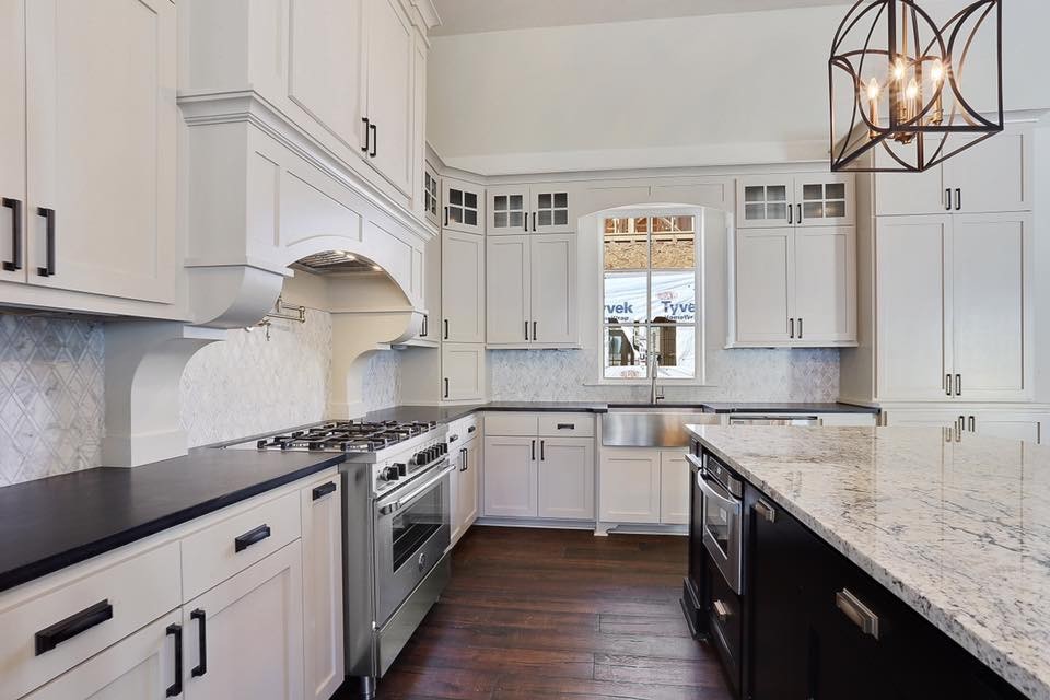 Inspiration for a large transitional medium tone wood floor and brown floor kitchen remodel in New Orleans with a farmhouse sink, recessed-panel cabinets, white cabinets, granite countertops, gray backsplash, mosaic tile backsplash, stainless steel appliances and an island