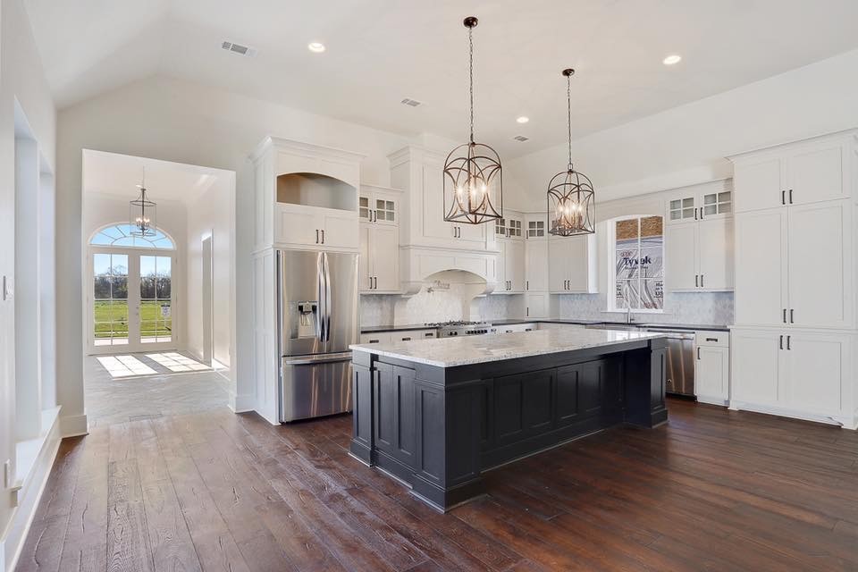 Example of a large transitional l-shaped medium tone wood floor and brown floor kitchen design in New Orleans with a farmhouse sink, recessed-panel cabinets, white cabinets, granite countertops, gray backsplash, mosaic tile backsplash, stainless steel appliances and an island