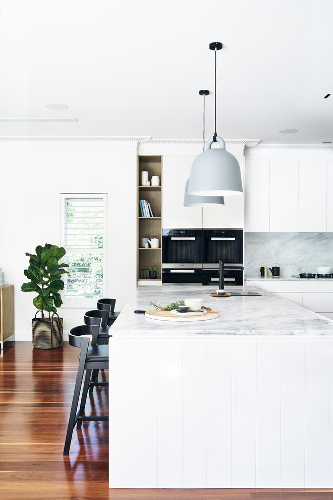 Design ideas for a large scandinavian l-shaped open plan kitchen in Sydney with flat-panel cabinets, white cabinets, marble worktops, white splashback, stone slab splashback, stainless steel appliances, medium hardwood flooring, an island and brown floors.