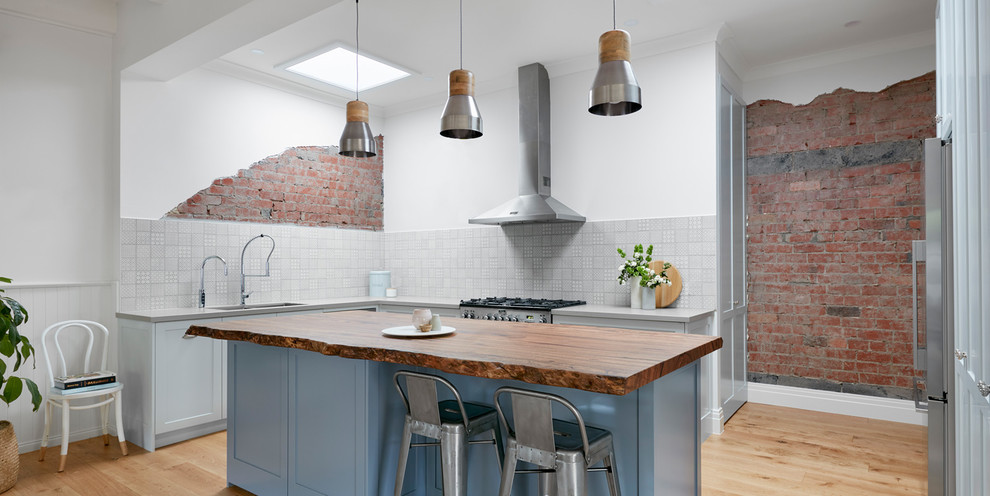 Industriell inredning av ett stort kök, med en dubbel diskho, luckor med infälld panel, blå skåp, träbänkskiva, stänkskydd i mosaik, rostfria vitvaror och en köksö