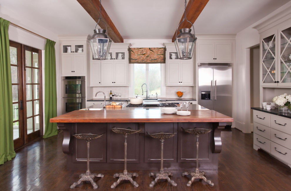 Cette image montre une grande cuisine américaine parallèle traditionnelle avec un évier de ferme, une crédence blanche, un électroménager en acier inoxydable, un sol en bois brun et îlot.