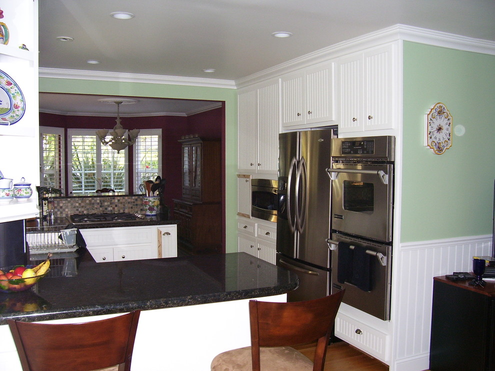 Foto på ett mellanstort vintage kök, med en dubbel diskho, skåp i shakerstil, vita skåp, granitbänkskiva, flerfärgad stänkskydd, stänkskydd i stenkakel, rostfria vitvaror, mörkt trägolv, en halv köksö och brunt golv