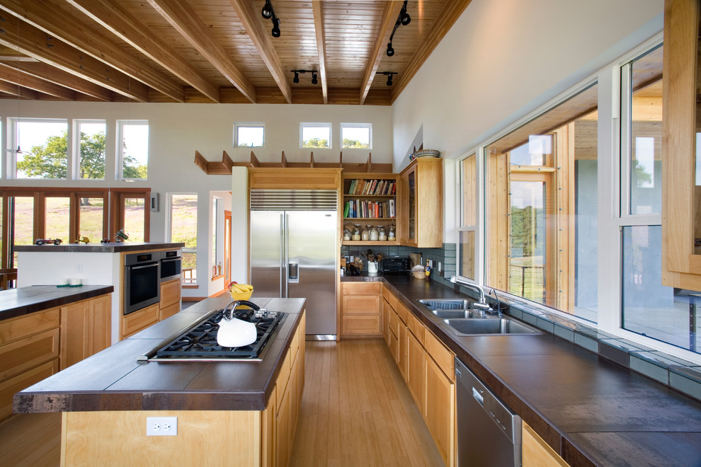 Bild på ett stort funkis kök, med rostfria vitvaror, en trippel diskho, skåp i mellenmörkt trä, stänkskydd i keramik, mellanmörkt trägolv, en köksö, luckor med infälld panel, flerfärgad stänkskydd och brunt golv