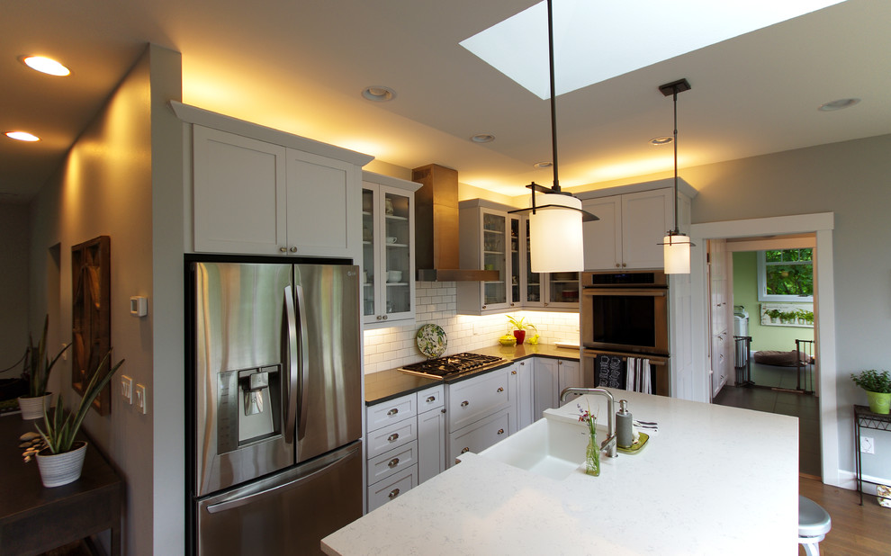Bild på ett mellanstort funkis vit vitt kök, med en nedsänkt diskho, luckor med glaspanel, vita skåp, marmorbänkskiva, vitt stänkskydd, stänkskydd i porslinskakel, rostfria vitvaror, mellanmörkt trägolv, en köksö och brunt golv