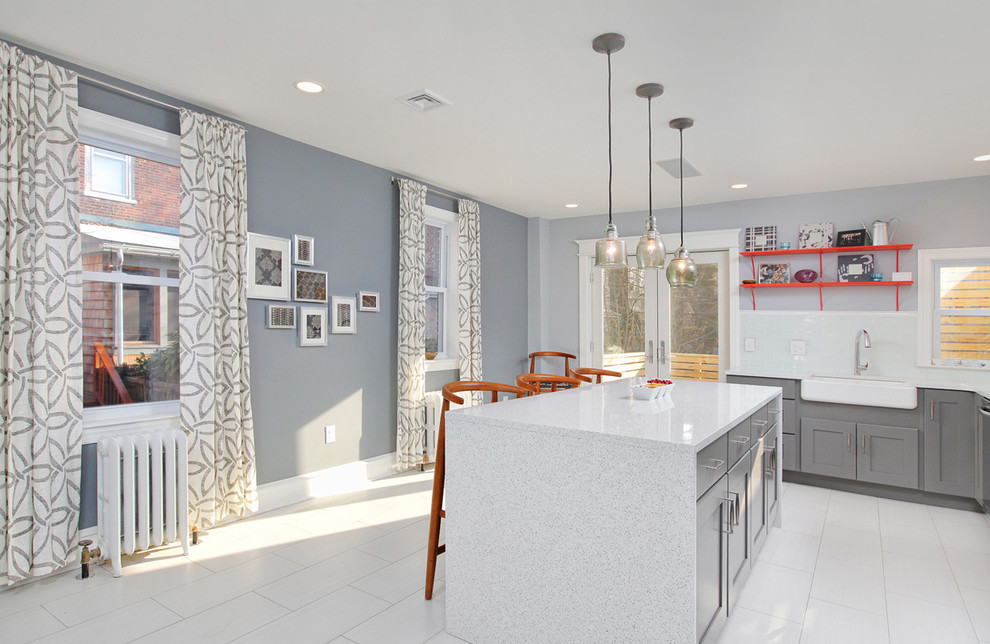 Large modern l-shaped kitchen/diner in Philadelphia with a belfast sink, grey cabinets, white splashback, an island, shaker cabinets, engineered stone countertops, metro tiled splashback, stainless steel appliances and porcelain flooring.
