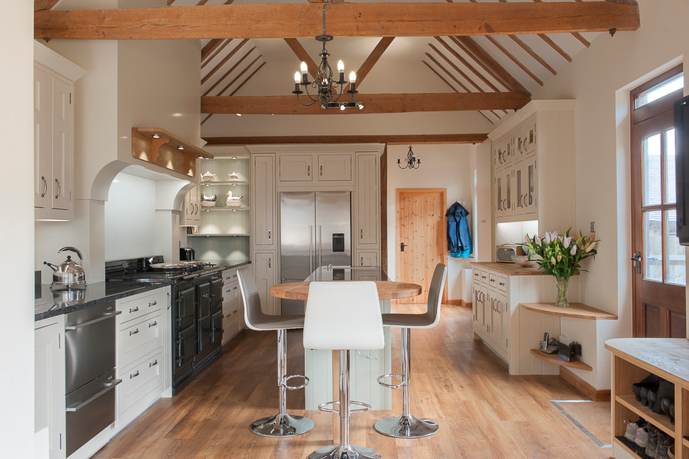 Country Küche mit Schrankfronten mit vertiefter Füllung, weißen Schränken, Küchengeräten aus Edelstahl, braunem Holzboden und Kücheninsel in Kent