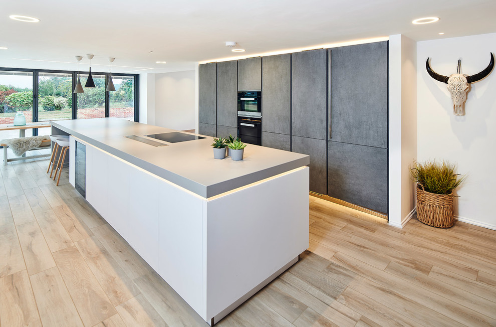Inspiration for a large country single-wall kitchen in Hertfordshire with flat-panel cabinets, grey cabinets, black appliances, light hardwood flooring, an island, beige floors and grey worktops.