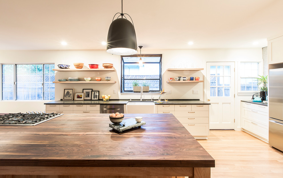 Moderne Wohnküche mit Landhausspüle, weißen Schränken, Küchengeräten aus Edelstahl, hellem Holzboden und Kücheninsel in Santa Barbara