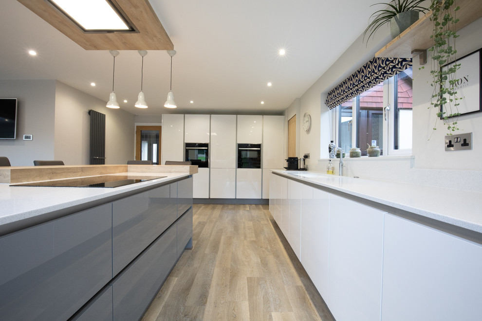 Example of a trendy l-shaped medium tone wood floor and brown floor kitchen design in Hampshire with an undermount sink, flat-panel cabinets, white cabinets, white backsplash, paneled appliances, an island and white countertops
