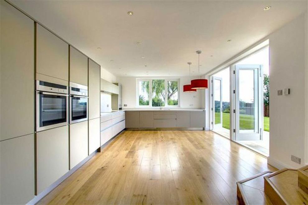 Medium sized contemporary l-shaped kitchen/diner in Surrey with a double-bowl sink, flat-panel cabinets, beige cabinets, stainless steel appliances, light hardwood flooring and no island.