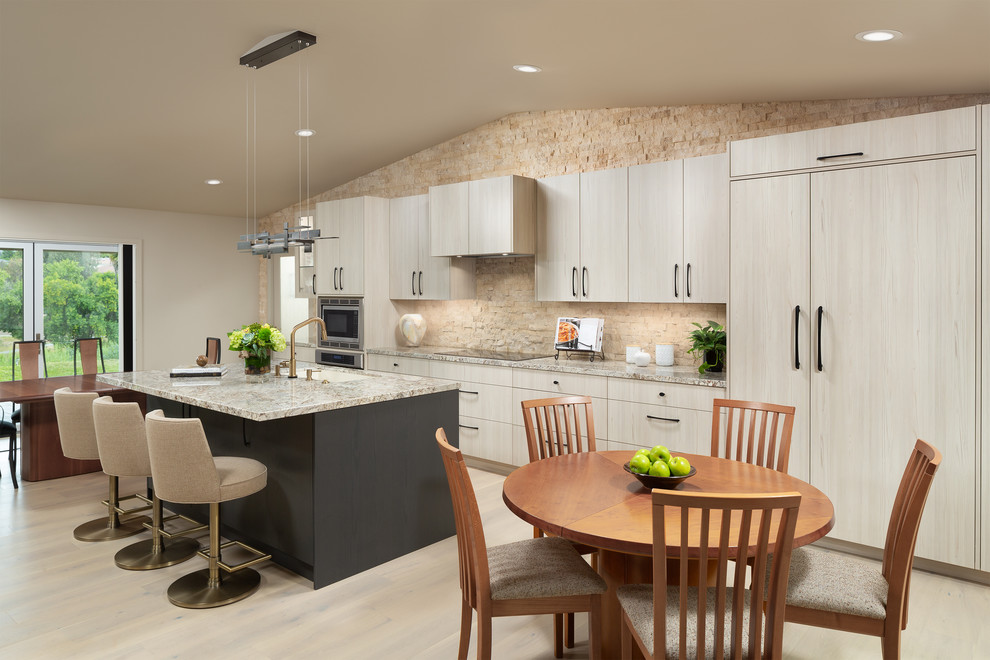 Example of a mid-sized trendy single-wall light wood floor and beige floor open concept kitchen design in Orange County with a double-bowl sink, flat-panel cabinets, light wood cabinets, granite countertops, beige backsplash, marble backsplash, paneled appliances, an island and beige countertops