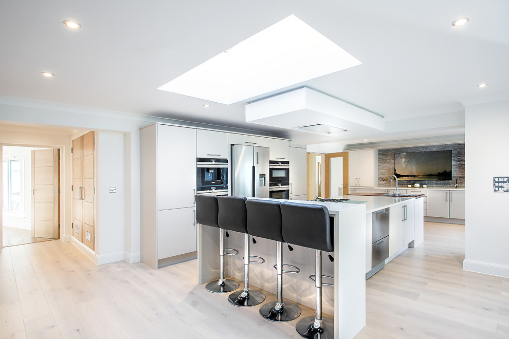 Photo of a large contemporary kitchen in Hampshire with flat-panel cabinets, grey cabinets, grey splashback, stainless steel appliances, light hardwood flooring, multiple islands, beige floors and white worktops.