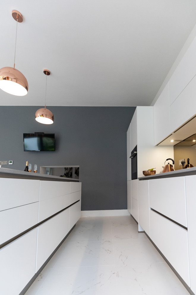 Mid-sized minimalist galley porcelain tile and white floor eat-in kitchen photo in Hampshire with a single-bowl sink, flat-panel cabinets, white cabinets, quartzite countertops, metallic backsplash, glass sheet backsplash, paneled appliances, an island and gray countertops
