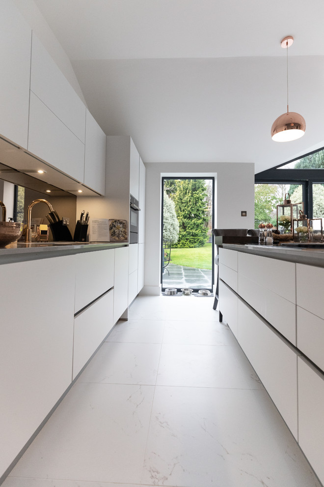 Modern inredning av ett mellanstort grå grått kök, med en enkel diskho, släta luckor, vita skåp, bänkskiva i kvartsit, stänkskydd med metallisk yta, glaspanel som stänkskydd, integrerade vitvaror, klinkergolv i porslin, en köksö och vitt golv
