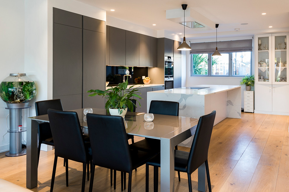 This is an example of a medium sized contemporary single-wall open plan kitchen in London with grey cabinets, composite countertops, black splashback, glass sheet splashback, integrated appliances and an island.