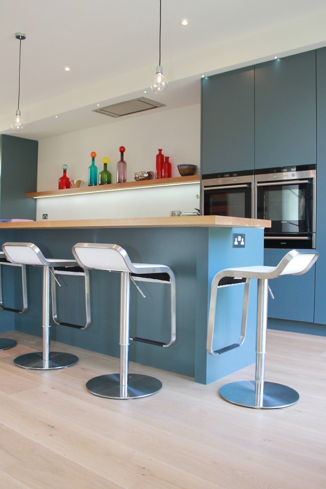 Mittelgroße Moderne Wohnküche mit Unterbauwaschbecken, flächenbündigen Schrankfronten, blauen Schränken, Quarzwerkstein-Arbeitsplatte, Küchenrückwand in Weiß, hellem Holzboden und Kücheninsel in London