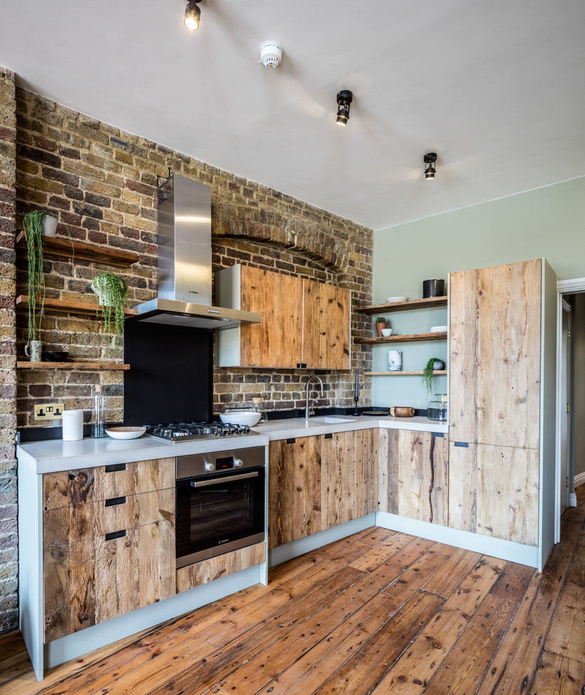 ロンドンにある高級な小さなラスティックスタイルのおしゃれなキッチン (フラットパネル扉のキャビネット、中間色木目調キャビネット、茶色いキッチンパネル、レンガのキッチンパネル、無垢フローリング、アイランドなし、コンクリートカウンター、シルバーの調理設備) の写真