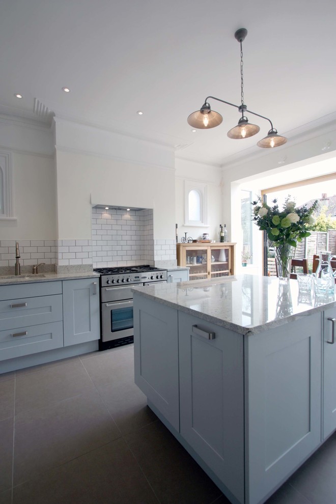 This is an example of a large classic l-shaped kitchen/diner in London with a submerged sink, shaker cabinets, blue cabinets, granite worktops, white splashback, ceramic splashback, stainless steel appliances, porcelain flooring and an island.