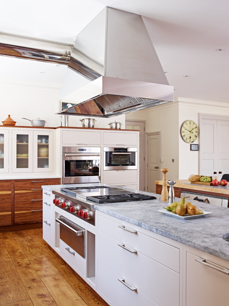 Foto di un'ampia cucina design con ante lisce, elettrodomestici in acciaio inossidabile, 2 o più isole, ante bianche, pavimento in legno massello medio e top in marmo