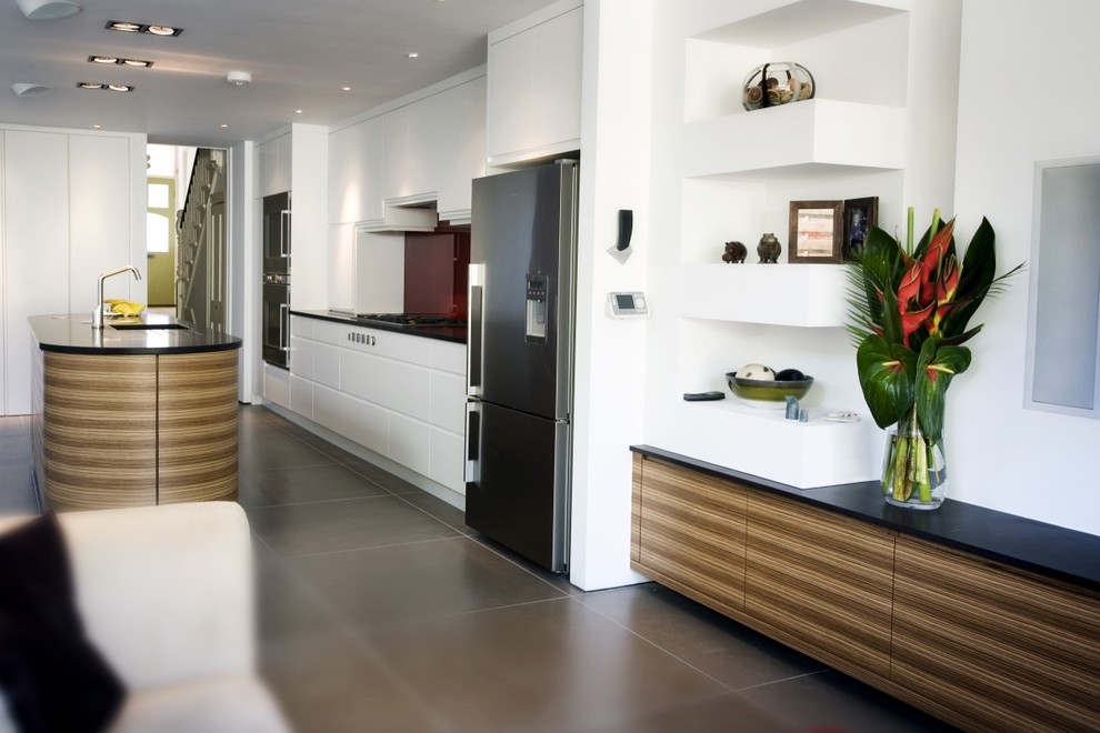 Large contemporary u-shaped open plan kitchen in London with a submerged sink, flat-panel cabinets, medium wood cabinets, wood worktops, metallic splashback, stainless steel appliances, ceramic flooring and an island.